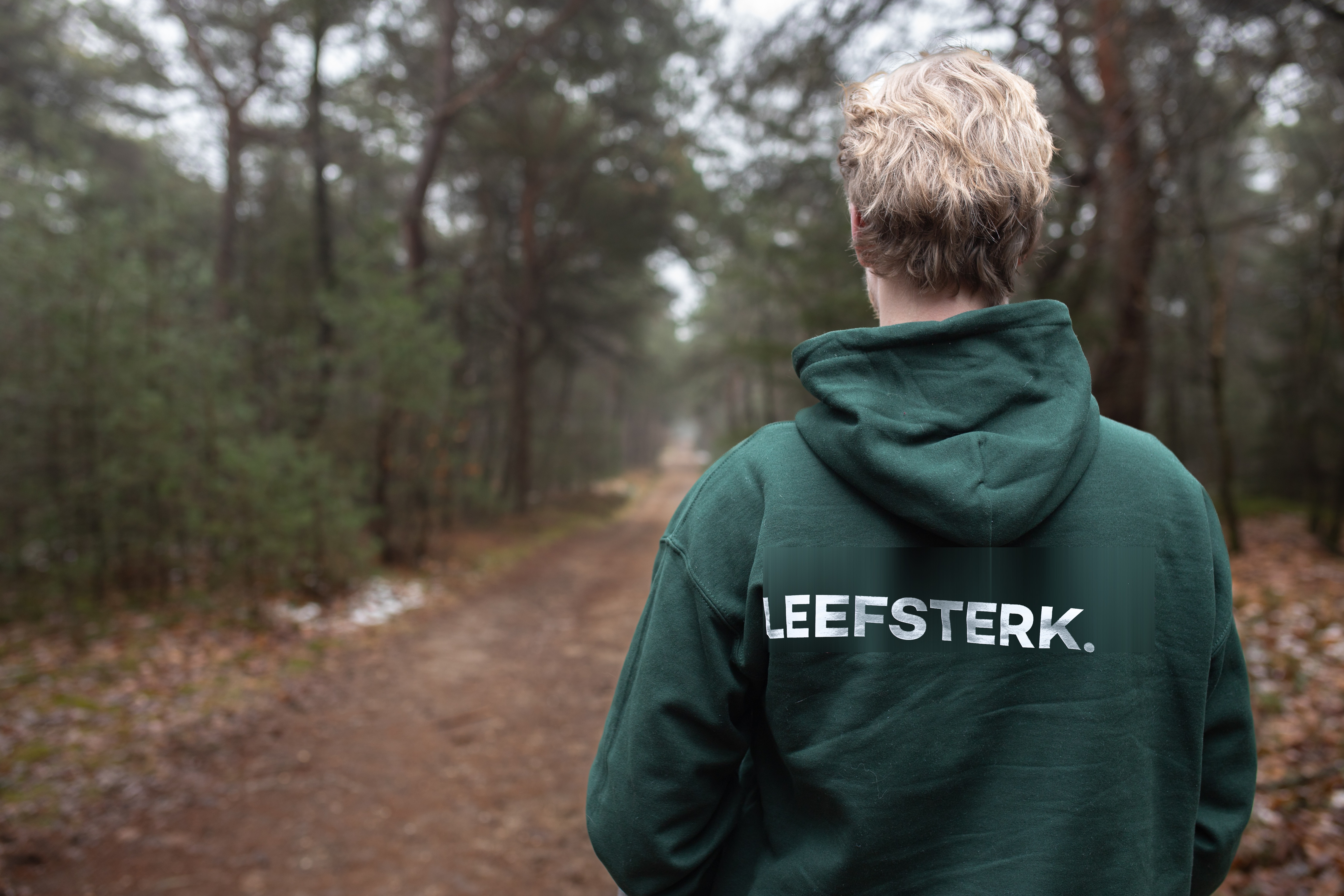 Persoon in Leefsterk hoodie kijkt over bospad in de mist